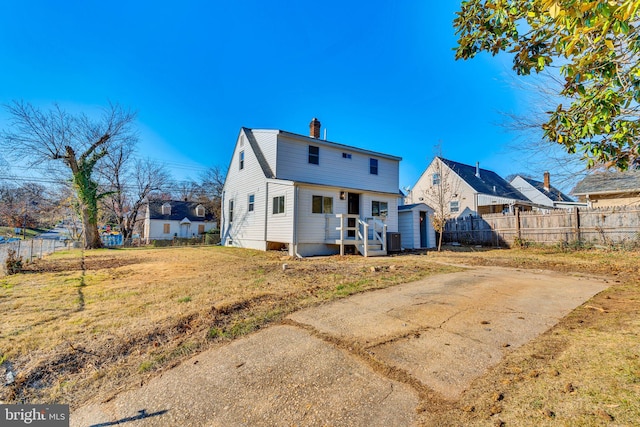 rear view of house featuring a lawn, a chimney, and fence