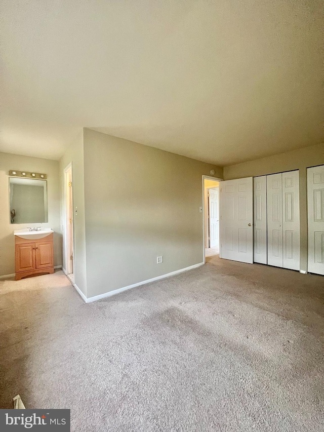 unfurnished bedroom featuring two closets, ensuite bathroom, a sink, carpet, and baseboards