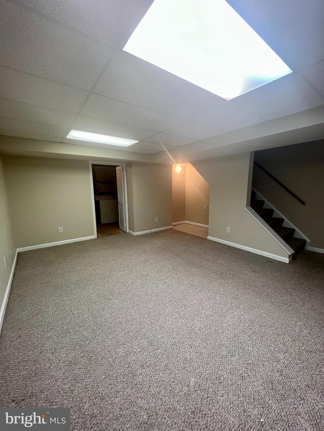 finished below grade area with stairway, a paneled ceiling, baseboards, and carpet floors