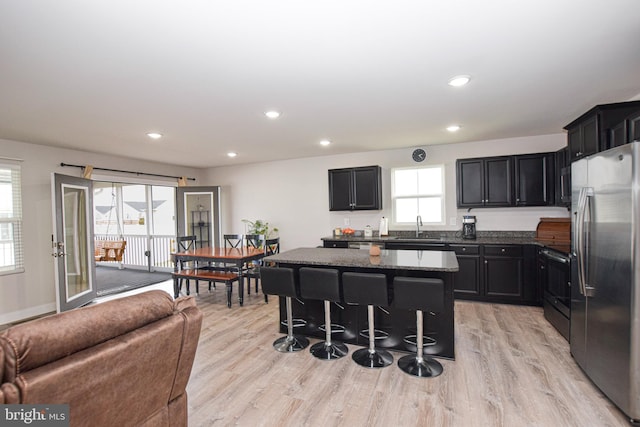 kitchen featuring light wood finished floors, a center island, dark stone counters, stainless steel appliances, and a sink