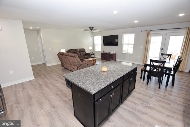 kitchen with light wood-style flooring, a kitchen island, dark cabinetry, and a ceiling fan