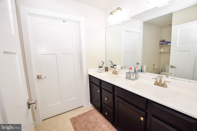 bathroom featuring tile patterned floors, toilet, double vanity, and a sink