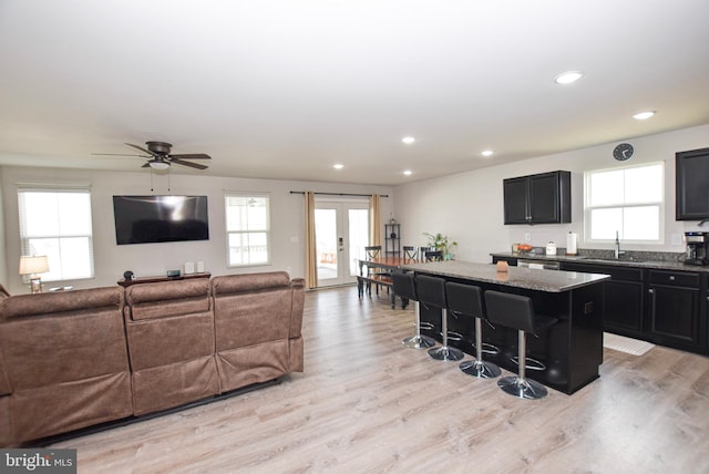 kitchen with a kitchen island, open floor plan, a kitchen bar, light wood-type flooring, and stone counters