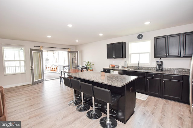 kitchen with light stone countertops, a breakfast bar, light wood-style flooring, a sink, and a center island