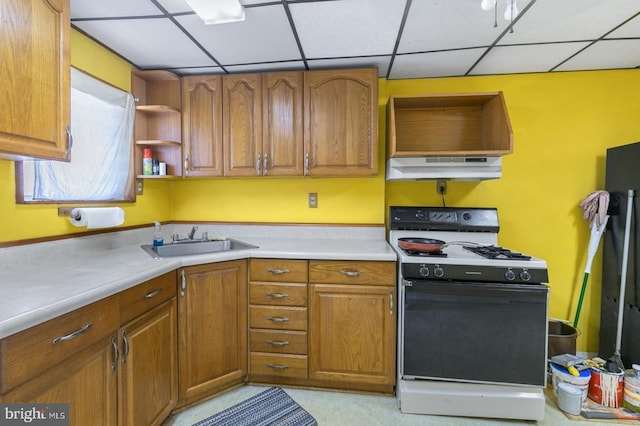 kitchen with under cabinet range hood, a sink, brown cabinetry, and gas range oven