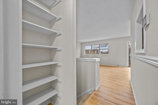 hallway with an upstairs landing, baseboards, and wood finished floors