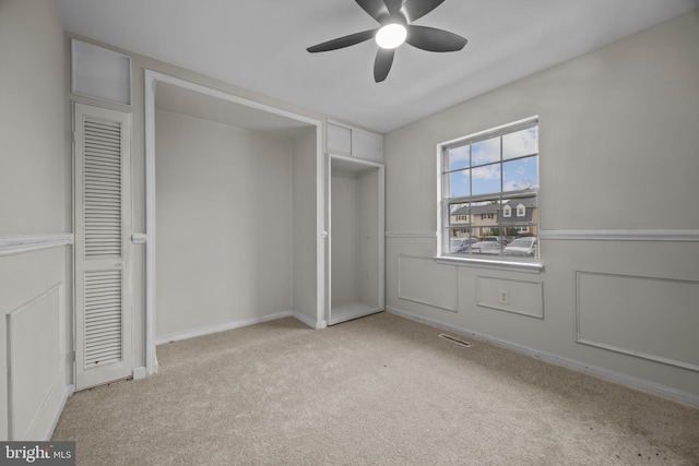 unfurnished bedroom with visible vents, a wainscoted wall, a ceiling fan, carpet flooring, and a decorative wall