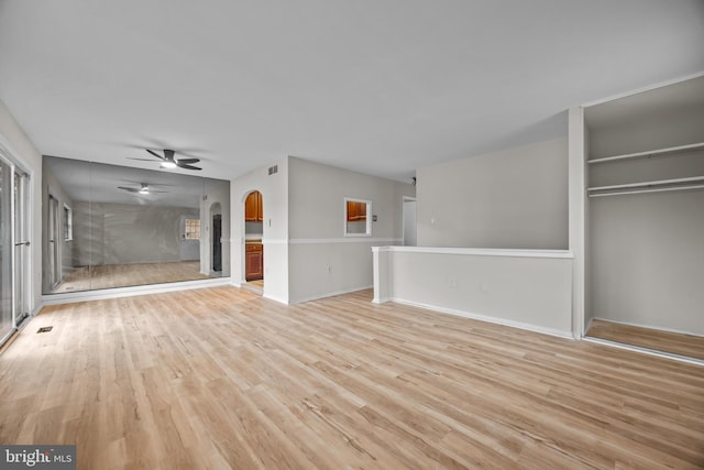 unfurnished living room with baseboards, visible vents, light wood finished floors, arched walkways, and ceiling fan