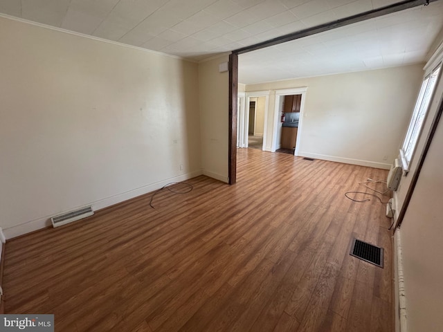 spare room featuring crown molding, wood finished floors, visible vents, and baseboards