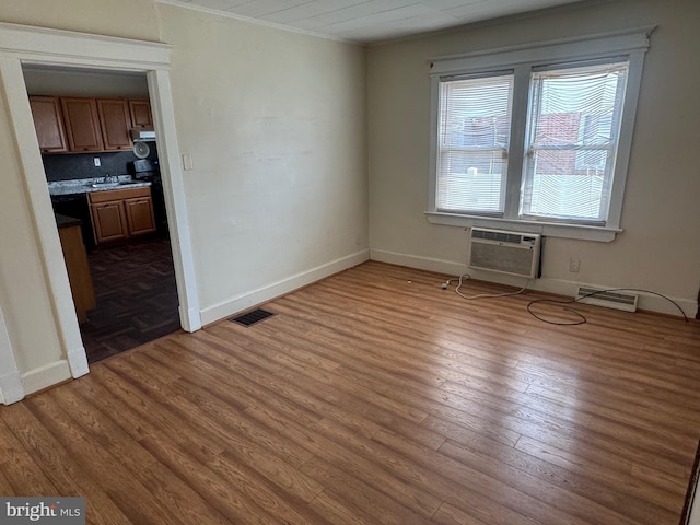 empty room featuring ornamental molding, wood finished floors, visible vents, and a wall mounted AC