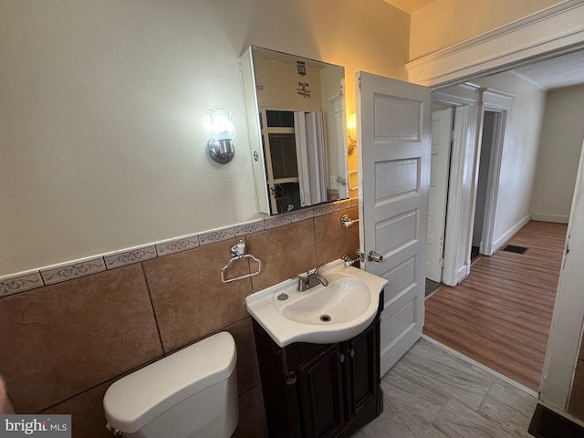 half bath featuring vanity, a wainscoted wall, visible vents, tile walls, and toilet