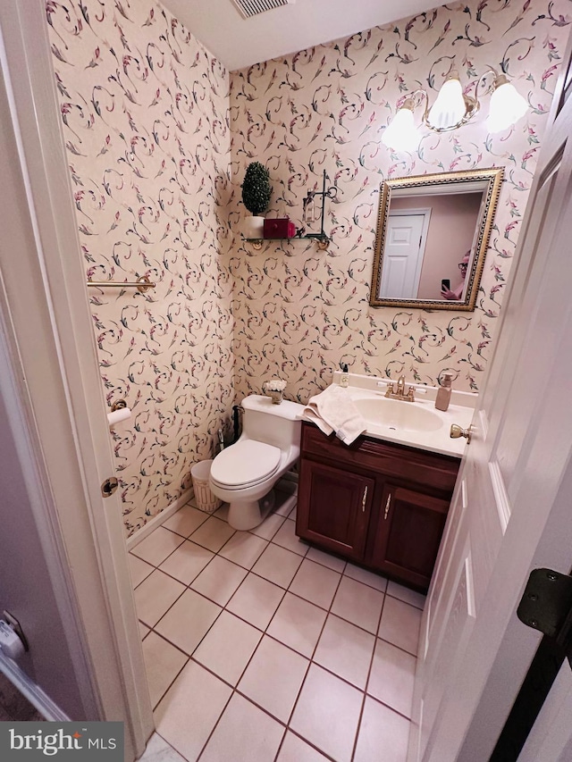 half bath featuring vanity, visible vents, wallpapered walls, tile patterned floors, and toilet