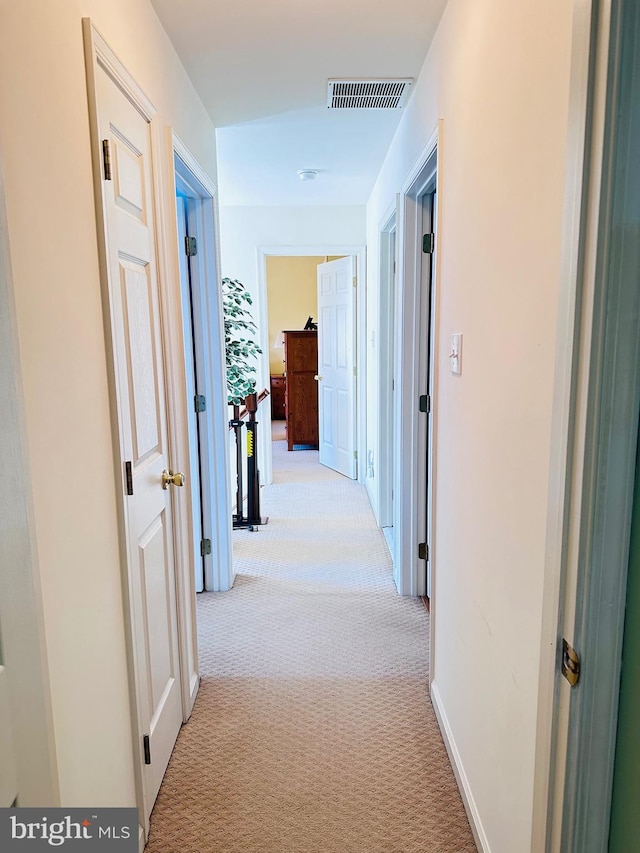 hall featuring light colored carpet, visible vents, and baseboards