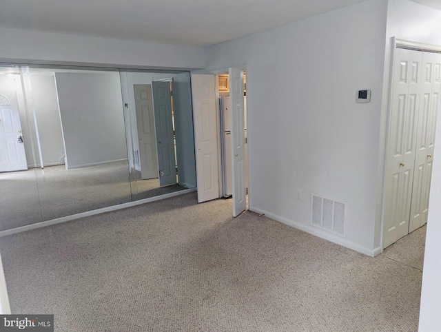 unfurnished bedroom featuring visible vents, two closets, freestanding refrigerator, carpet, and baseboards