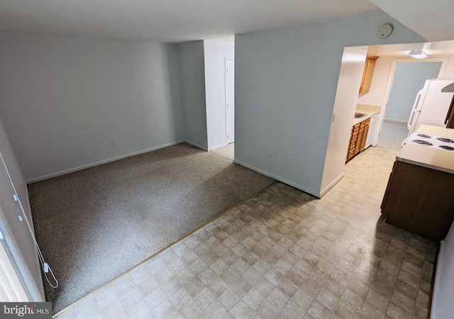 interior space featuring light floors, baseboards, freestanding refrigerator, light countertops, and light carpet