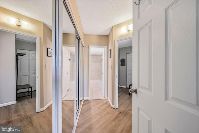 hallway with baseboards, a textured ceiling, and light wood-style floors