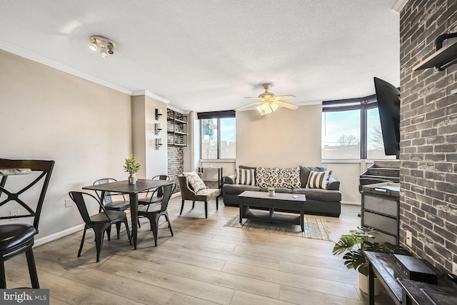 living area featuring light wood-type flooring, ornamental molding, a ceiling fan, a textured ceiling, and baseboards