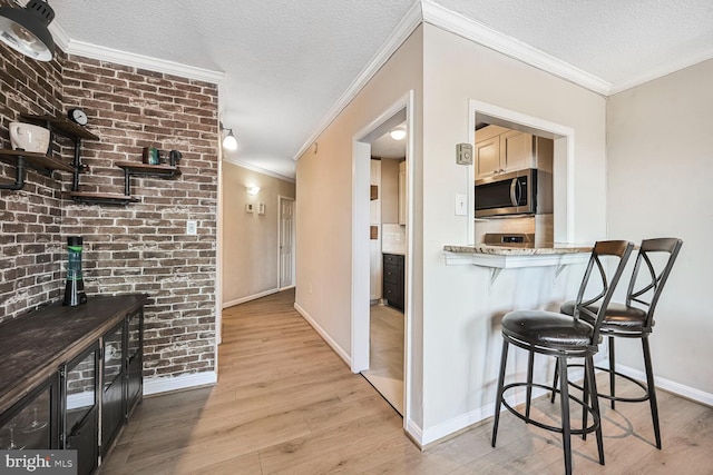 kitchen featuring stainless steel microwave, a textured ceiling, light wood-style floors, and ornamental molding