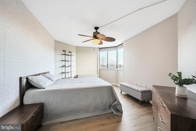 bedroom with a ceiling fan, wood finished floors, and brick wall