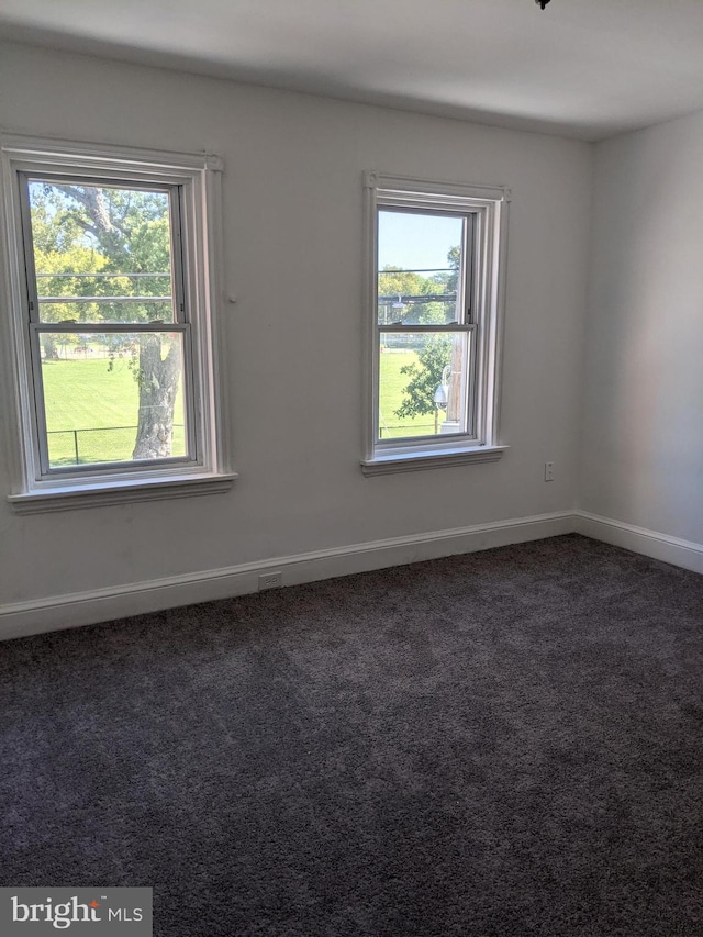 spare room featuring dark colored carpet and baseboards