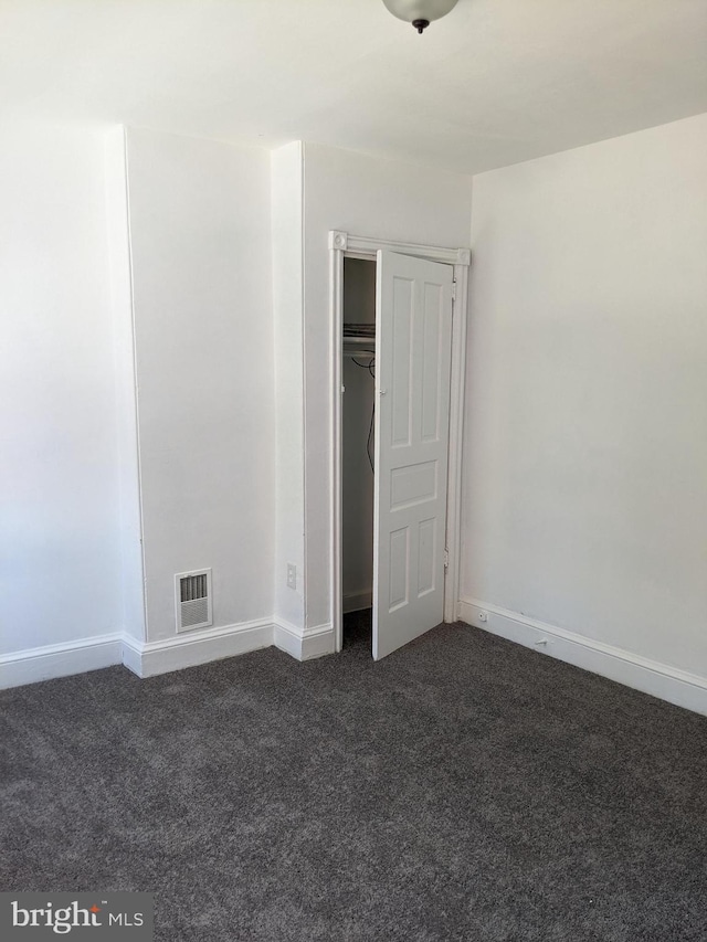 unfurnished bedroom featuring a closet, visible vents, baseboards, and dark colored carpet