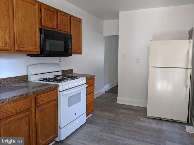 kitchen with dark countertops, baseboards, brown cabinets, white appliances, and dark wood-style flooring