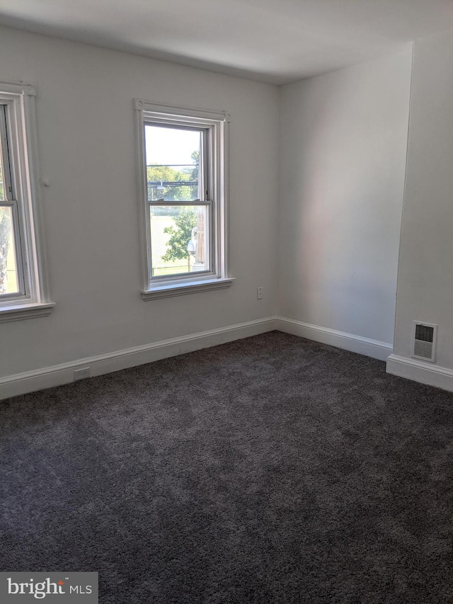 spare room featuring baseboards, visible vents, and dark carpet