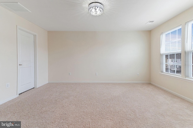 carpeted spare room with a notable chandelier, baseboards, and visible vents