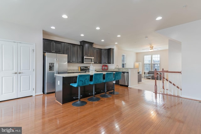 kitchen with light wood-type flooring, a breakfast bar, a center island with sink, recessed lighting, and appliances with stainless steel finishes