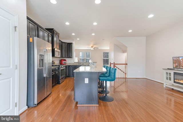 kitchen with recessed lighting, appliances with stainless steel finishes, a kitchen breakfast bar, light wood-style floors, and a ceiling fan