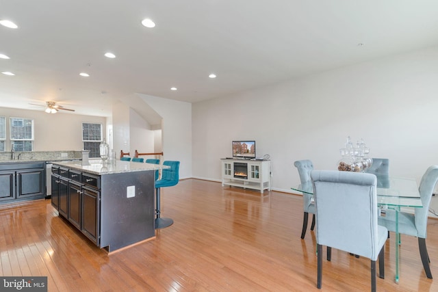 kitchen with a kitchen bar, light wood-style flooring, a center island, recessed lighting, and light stone countertops