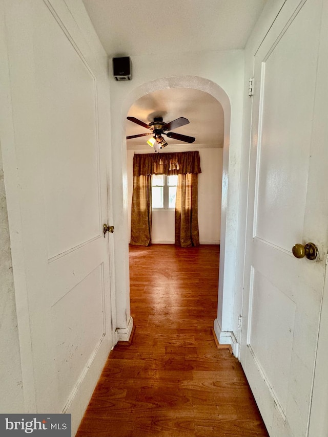 hall with wood finished floors, baseboards, and arched walkways