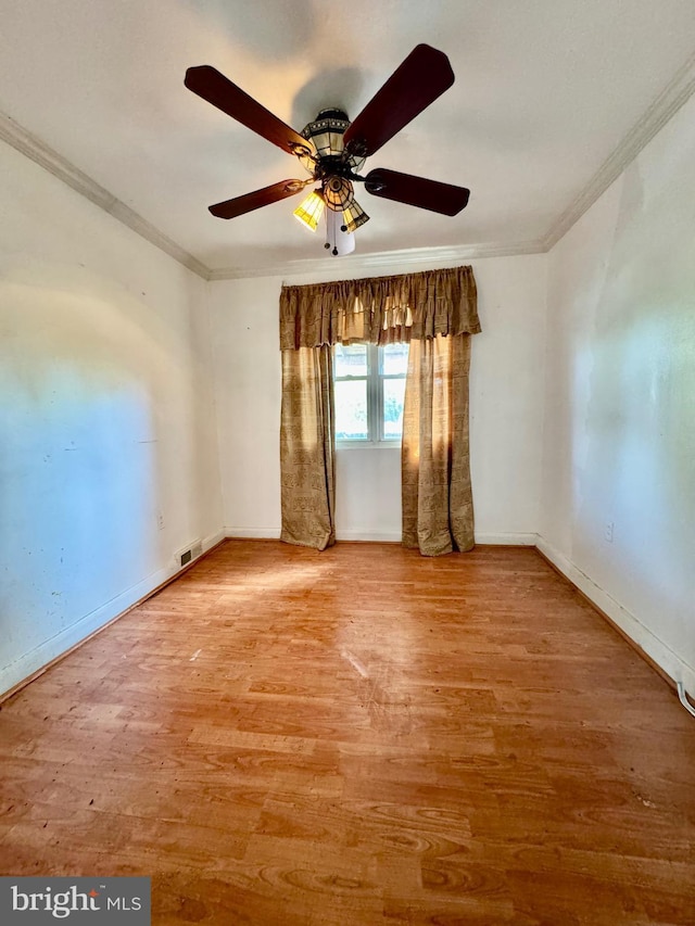 empty room with crown molding, a ceiling fan, visible vents, and wood finished floors