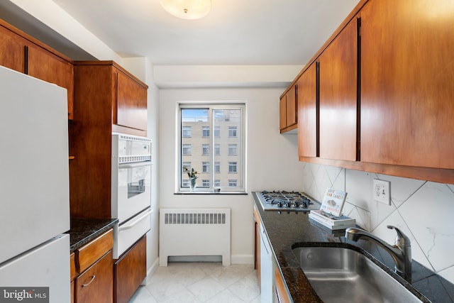 kitchen with white appliances, brown cabinetry, radiator heating unit, a sink, and tasteful backsplash