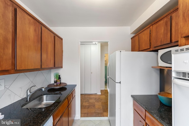 kitchen with backsplash, dark stone counters, freestanding refrigerator, brown cabinetry, and a sink