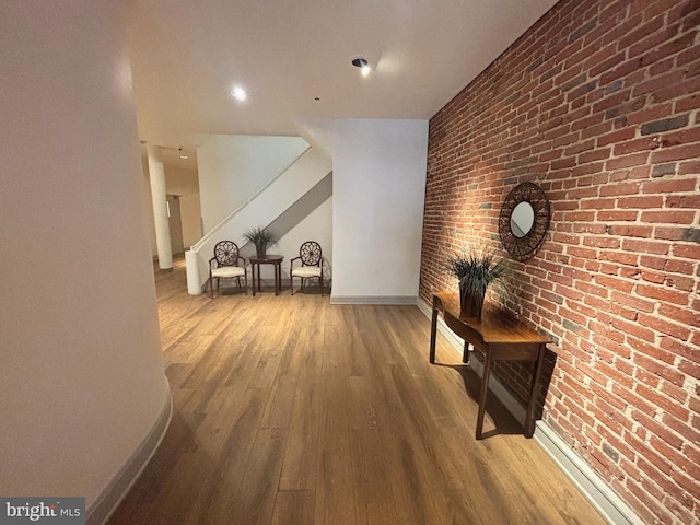 corridor featuring stairs, wood finished floors, baseboards, and brick wall