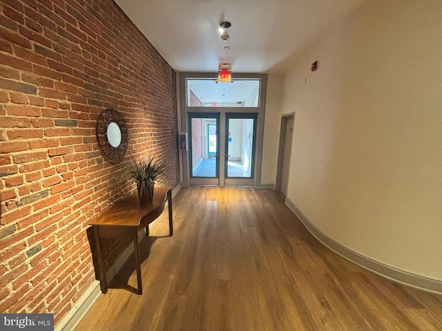 hallway featuring wood finished floors, baseboards, and brick wall