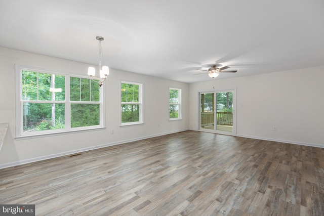 empty room featuring visible vents, ceiling fan with notable chandelier, baseboards, and wood finished floors