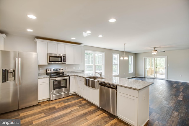 kitchen featuring a sink, light stone counters, appliances with stainless steel finishes, a peninsula, and white cabinets