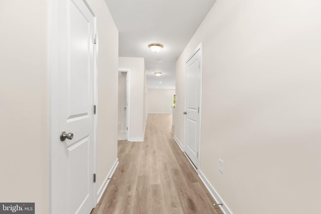 corridor with light wood-type flooring and baseboards