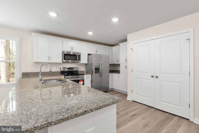 kitchen with a sink, white cabinetry, stainless steel appliances, light wood finished floors, and light stone countertops