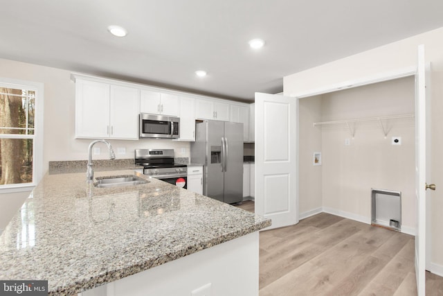 kitchen featuring light stone countertops, light wood-style flooring, a sink, appliances with stainless steel finishes, and white cabinetry