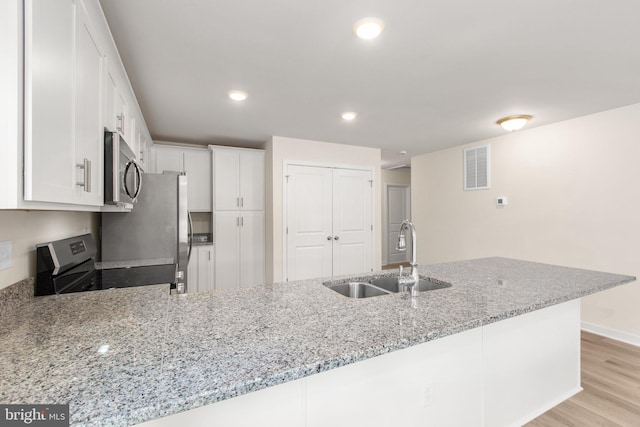 kitchen with visible vents, a sink, light stone counters, stainless steel appliances, and a peninsula