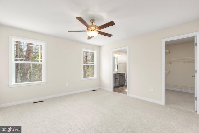 unfurnished bedroom with a spacious closet, visible vents, baseboards, carpet flooring, and ensuite bath