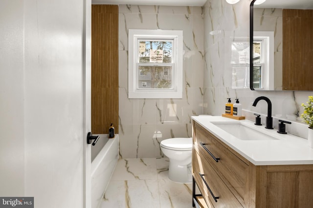 bathroom with tile walls, toilet, a bath, marble finish floor, and vanity