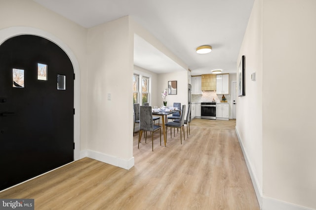 foyer entrance featuring baseboards, arched walkways, and light wood finished floors