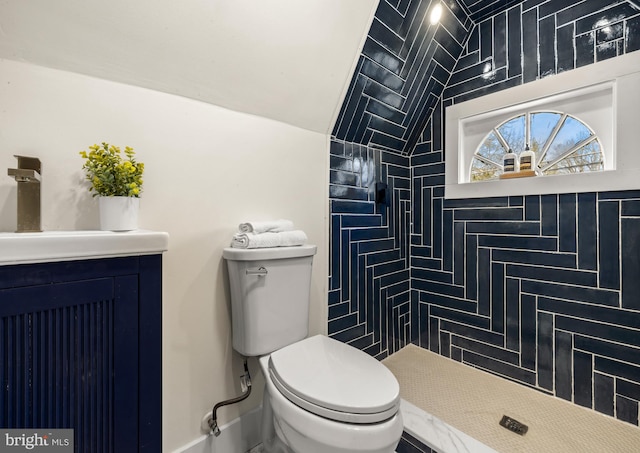 bathroom with toilet, a tile shower, baseboards, vanity, and vaulted ceiling