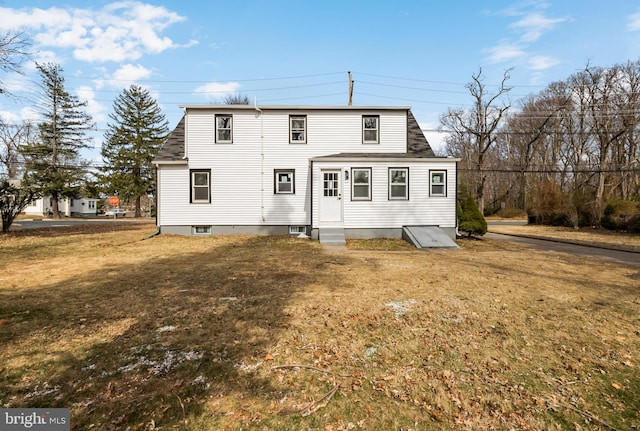 rear view of property featuring a lawn, entry steps, and a shingled roof