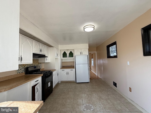 kitchen with backsplash, under cabinet range hood, freestanding refrigerator, white cabinets, and gas stove