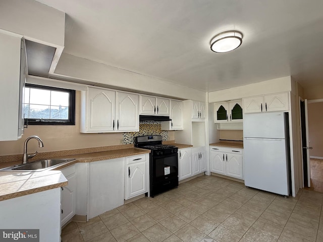 kitchen with black gas stove, under cabinet range hood, freestanding refrigerator, white cabinetry, and a sink